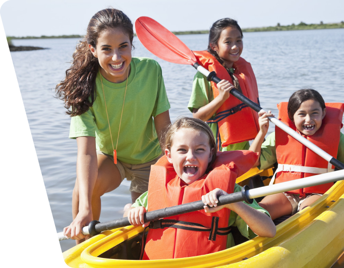Community Education Main Banner - 3 smiling children and 1 smiling chaperone in a shallow pond in a kayak.
